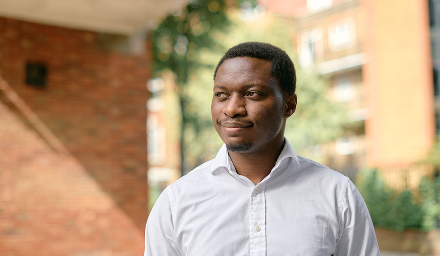 Dr Olu Tokode standing in front of trees and a building