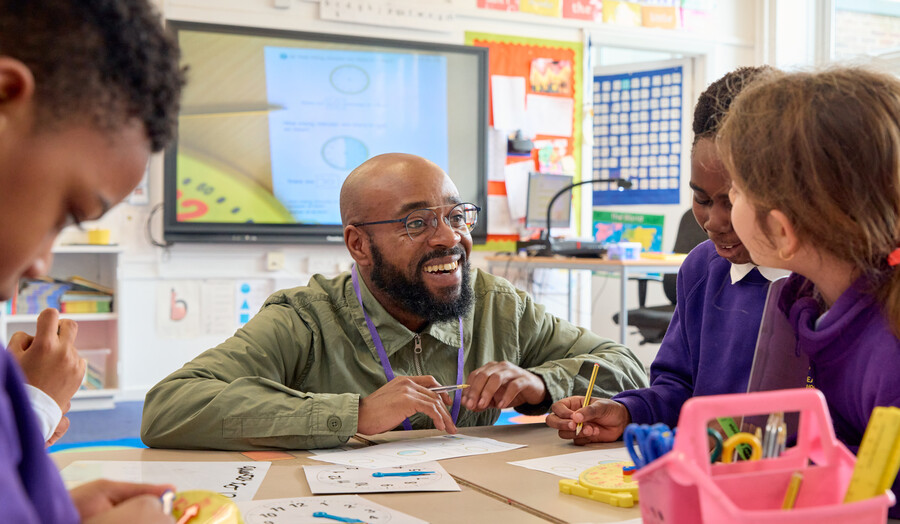 Teacher is at a table helping pupils in primary classroom