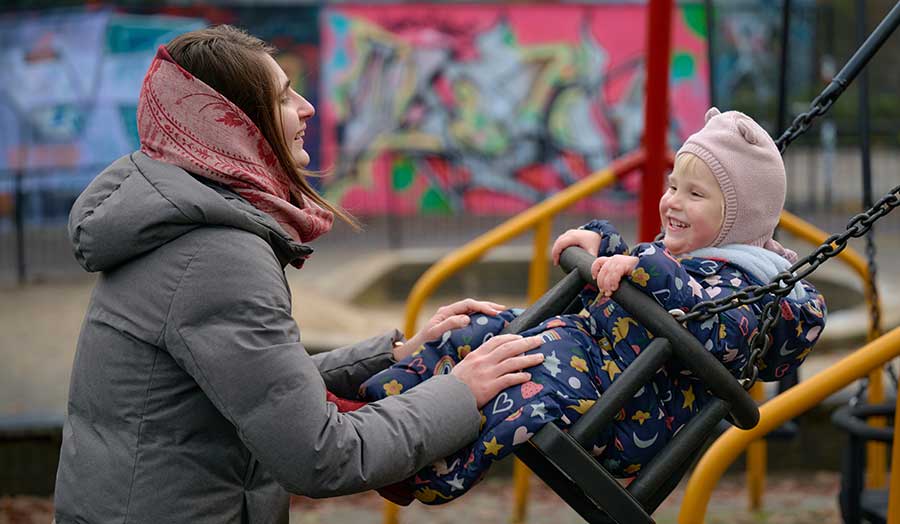 Stefani smiling at her daughter as she pushes her on the swing