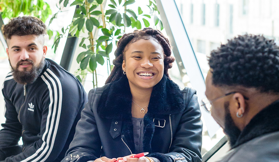 Smiling students sat inside the Graduate Centre with plant behind