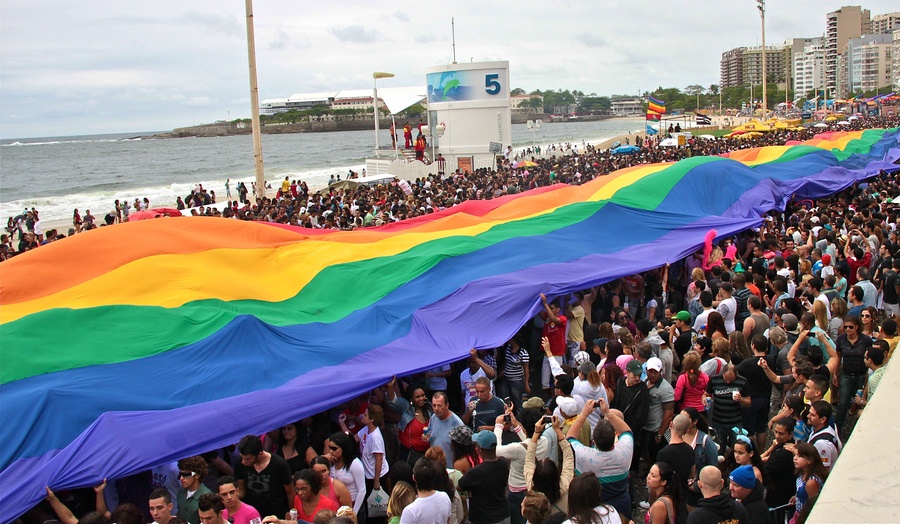thousands of people marching on a beach with a giant rainbow flag