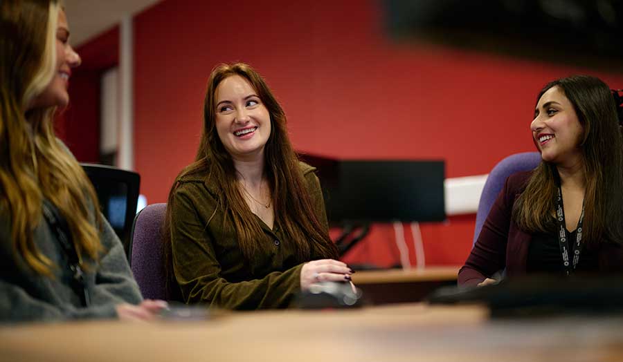 Three students smiling and chatting at a table