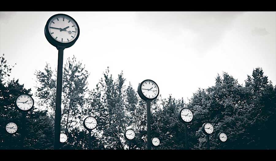 Several clocks attached to long poles, in front of a background of trees