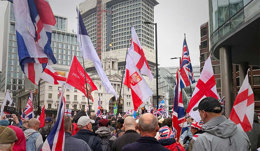 A crowd of people on a city street, holding flags including the Union Jack, St George's Cross, and Polish 'bandera' 
