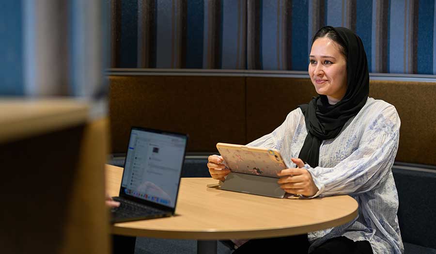 Isha pictured sitting at a desk with laptop, chatting to someone else