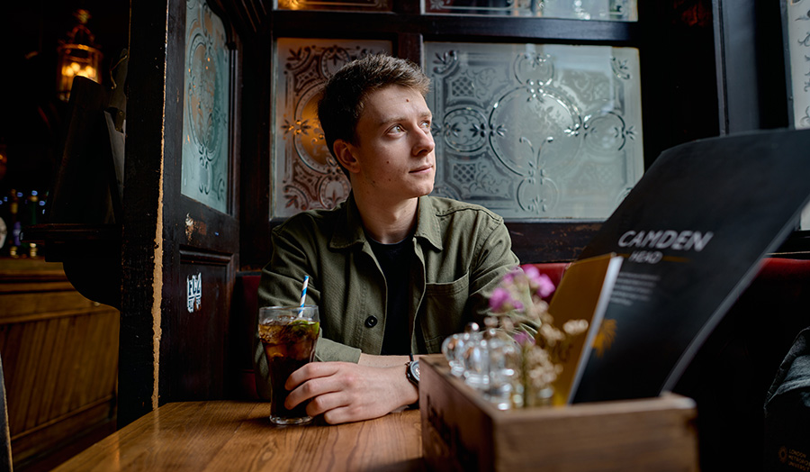 A person sitting in a dark pub with their hand on a glass